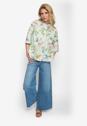 Koszula na guziki z krótkim rękawem w kolorze białym, ozdobiona żywymi liśćmi i wzorami zwierzęcymi. W zestawie z dżinsami o szerokich nogawkach.