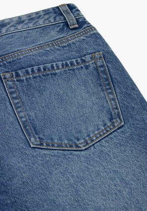 Modré džínsy z denimu so zadným vreckom a pútkom na opasok, zobrazujúce detailné oranžové prešívanie a textúru látky na bielom pozadí.