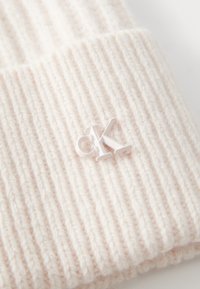 Berretto a maglia rosa chiaro con righe verticali. Caratterizzato da un piccolo logo "CK" bianco in plastica sulla piega. Texture morbida, design casual.