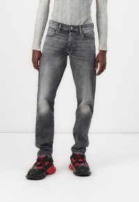 Jeans grises con un acabado desgastado, corte recto y diseño clásico de cinco bolsillos, combinados con zapatillas deportivas negras y rojas.