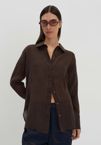 Brown button-up shirt with a soft, lightweight fabric, featuring a collar, long sleeves, and side slits for ease of movement.