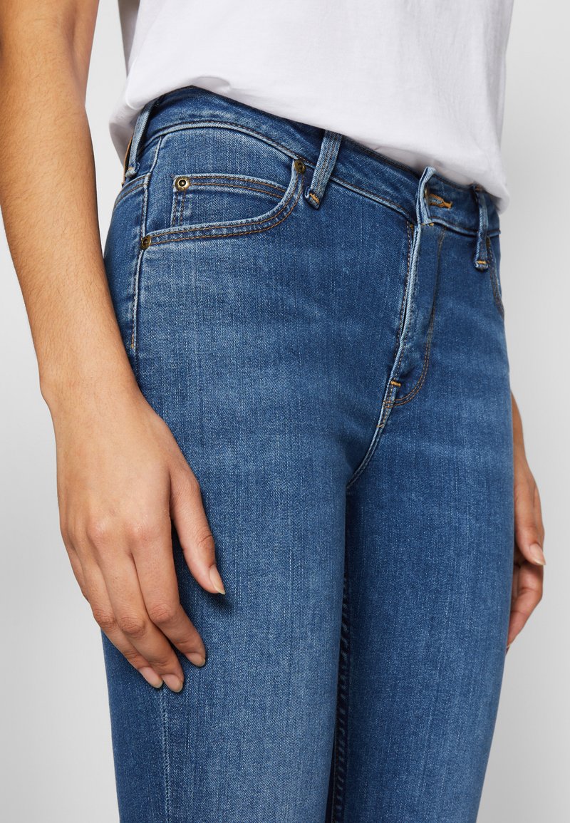 Niebieskie dżinsowe skinny jeansy z średnim stanem, z dodatkami w kolorze złotym, pięcioma kieszeniami oraz gładką, lekko wyblakłą teksturą.