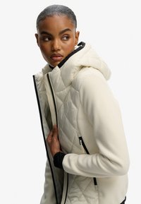 Biała pikowana kurtka z kapturem, charakteryzująca się gładkim materiałem i kontrastującymi czarnymi zamkami błyskawicznymi. Miękka tekstura i dopasowany krój.