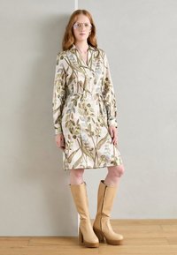 Rochie cu model floral, având frunze verzi și albastre pe un fundal bej, strânsă în talie cu un cordon. Botine bej cu platformă, până la genunchi.