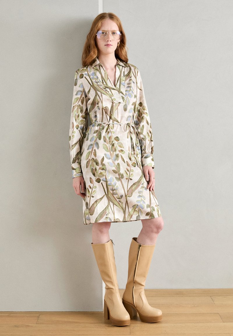 Rochie cu model floral, având frunze verzi și albastre pe un fundal bej, strânsă în talie cu un cordon. Botine bej cu platformă, până la genunchi.