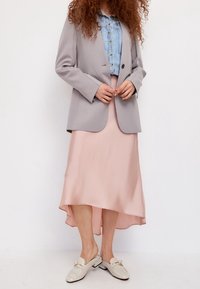 Hellgrauer Blazer über einem hellblauen Jeanshemd, kombiniert mit einem pinken asymmetrischen Rock und cremefarbenen Loafers mit einer Schleifendetail.