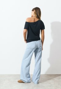 Top noir décolleté avec des manches courtes, associé à un jean bleu clair à jambes larges. Tissu doux avec une coupe décontractée.
