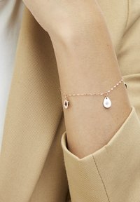 Rose gold bracelet with a delicate chain featuring two drop pendants, one engraved with a compass design and the other with a star pattern.