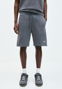 Pantaloni corti in cotone grigio con una vestibilità comoda, dotati di un cordino regolabile, tasche laterali e un piccolo logo bianco in basso a sinistra.