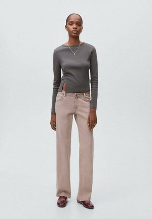 Woman wearing a fitted dark gray long-sleeve top with side slit, beige straight-leg pants, maroon shoes, and a necklace, standing on a plain background.