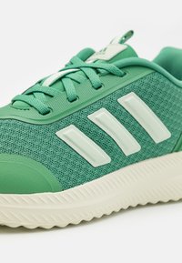 Chaussure de sport verte en mesh et en matériau synthétique. Présente trois rayures blanches, une semelle texturée et un bout de chaussure rond.