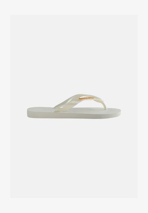 Bílá žabková sandál s texturovanou podrážkou a průhledným páskem se zlatou metalickou značkou na světlém pozadí.