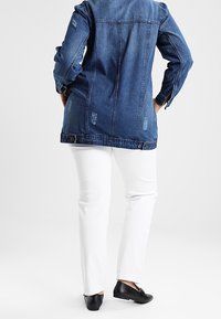 Jeansjacka med slitna detaljer, långa ärmar och knappmanschetter, i kombination med vita raka byxor och svarta ballerinas.