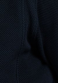 Textuur donkerblauwe stof met een subtiel gaasachtig patroon, met zichtbare stiksels en plooien, wat wijst op een zacht, flexibel materiaal.