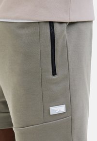 Grijze katoenen shorts met een zwarte ritszak, voorzien van een klein wit logo op de rechterpoot. Gladde textuur en een getailleerde pasvorm.