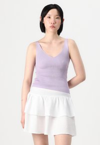 Lilla ribbet tank topp med dyp V-hals, kombinert med en hvit, lagdelt, volangskjørt laget av lett materiale.
