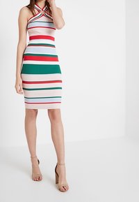 Robe tricotée ajustée avec un décolleté halter et un détail œillet. Motif à rayures rouge, vert et blanc. Mi-longue avec une texture côtelée.