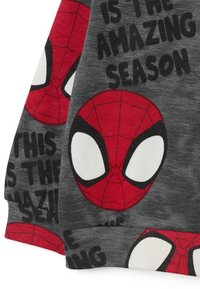 Grauer Baumwollstoff mit roten und schwarzen Spider-Man-Kopfdesigns und großen weißen Augen. Der Text lautet: "DAS IST DIE AMAZING SAISON."
