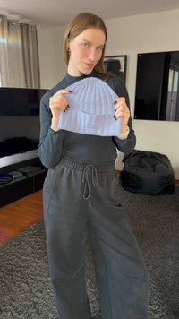 Vaaleansininen ribbineulottu pipo käsissä, jossa on käännetty reunus. Malli pukeutuneena mustaan poolopaitaan ja harmaisiin rentoihin housuihin.