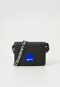 Černá taška přes rameno z texturovaného materiálu s modrým čtvercovým logem a popruhem s potiskem "KARL LAGERFELD".