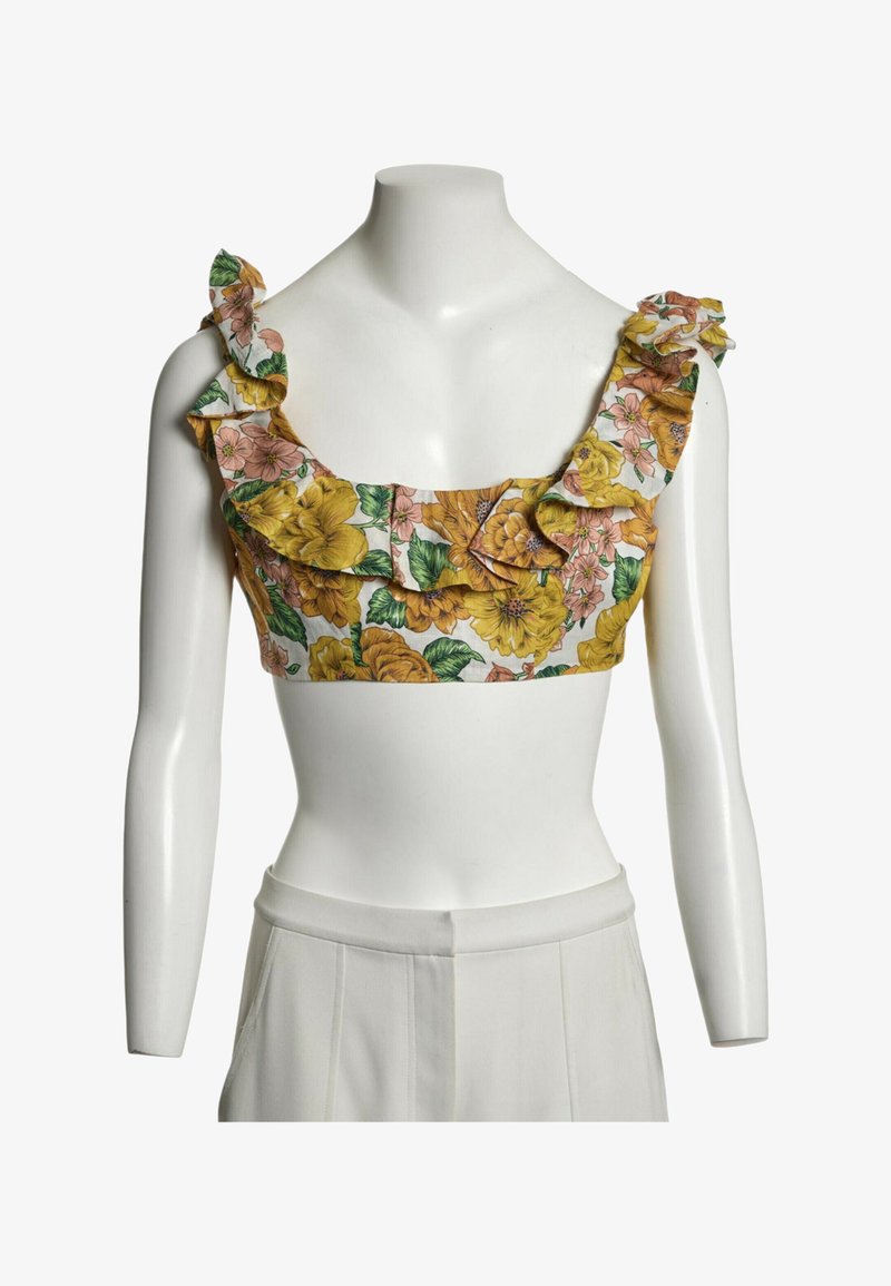 Crop top floral avec des fleurs jaunes et roses et des feuilles vertes, présentant des bretelles volantées et un décolleté carré sur un buste de mannequin blanc.