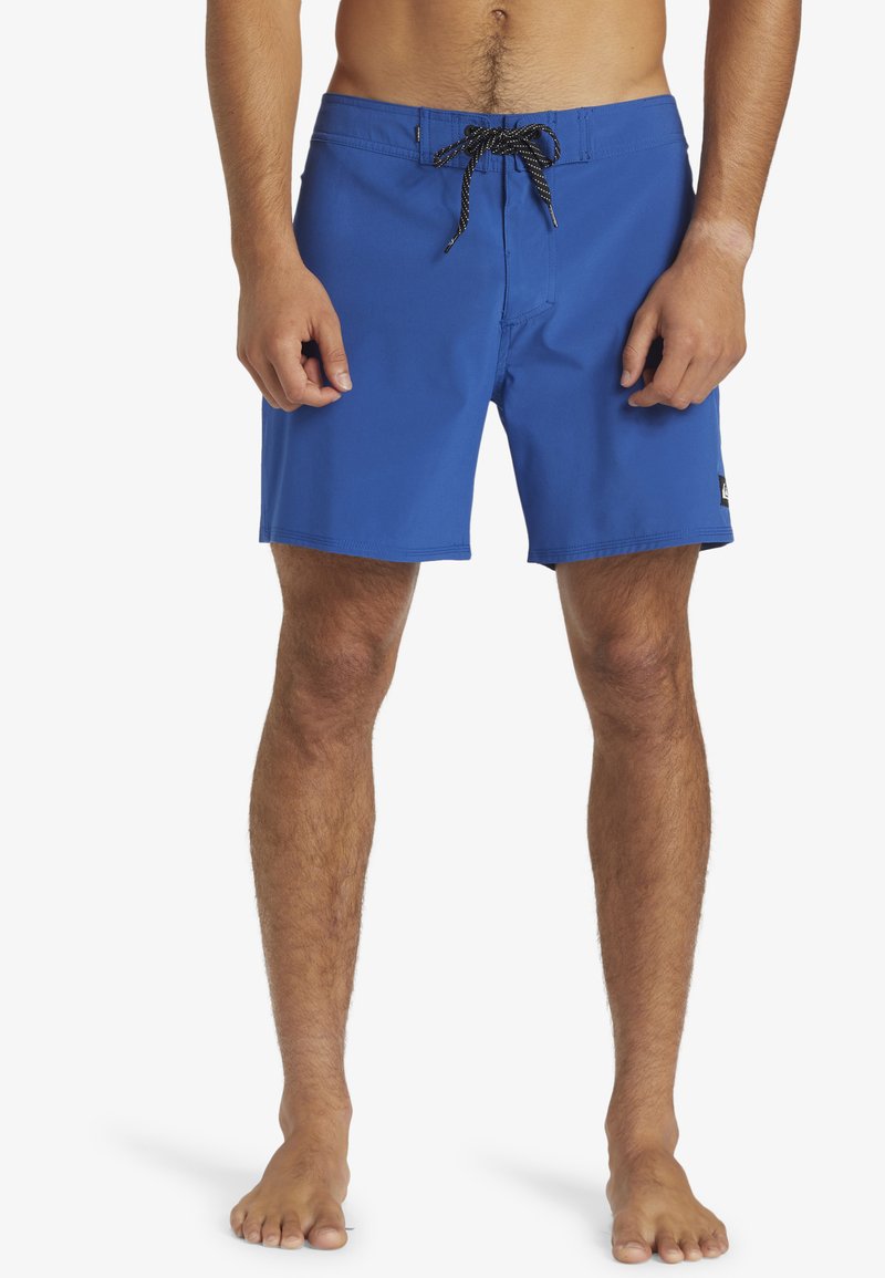 Shorts de înot albastre fabricate dintr-un material ușor. Acestea dispun de un sistem de închidere cu șnur, cu modele alb-negru și un logo mic pe lateral.