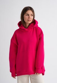 Heldere roze oversized hoodie met een grote voork pocket, een capuchon met trekkoord en geribbelde manchetten. Gemaakt van zachte, gestructureerde stof.