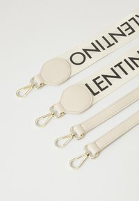Beige strap with bold black lettering; features gold hardware and leather accents; includes multiple attachment clips for versatility.