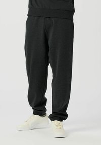 Črne trenirke z raztegljivim pasom in man�šetami, udobnega in sproščenega kroja. Kombinirane s belimi supergami z diskretnim logotipom.