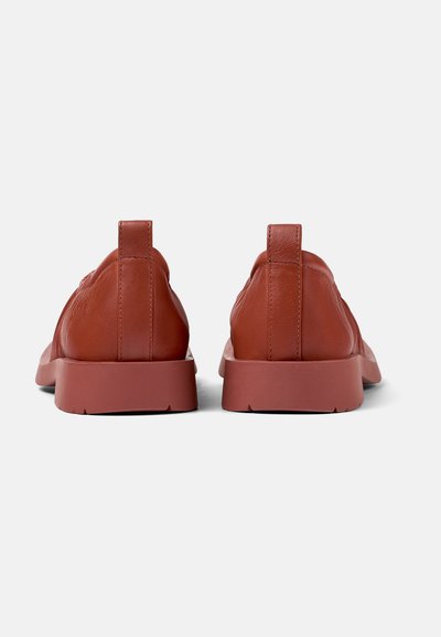 Brown leather sneakers with a smooth texture, minimalistic design, and a thick rubber sole. Features a small rear pull tab for easy wearing.