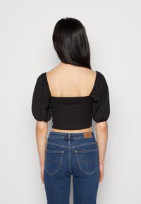 Svart kort topp med puffärmar och ribbat mönster. Matchas med blå, figursydda jeans i denim som har bakfickor och ett märke.