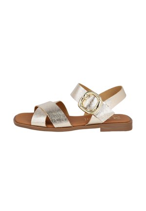 Sandalias metálicas doradas con suela plana, que cuentan con correas entrelazadas y un gran acento de hebilla. Superficie suave y diseño de parte trasera abierta.