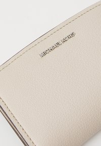 Portafoglio in pelle beige con superficie textured, bordi cuciti in alto e logo "MICHAEL KORS" in rilievo argentato sulla parte anteriore.