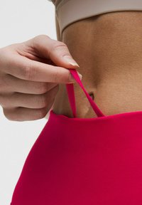 Svetlo roza aktivna majica s širokim izrezom in nastavljivimi naramnicami, ki je rahlo potegnjena, da razkrije ton kože. Gladka tekstura.