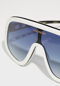 Occhiali da sole Carrera con montatura oversize bianca, dettagli neri e lenti blu sfumate. Presenta il logo del marchio in oro metallizzato sulla parte anteriore.