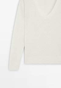 Maglione lavorato a maglia color crema con maniche lunghe e collo a V, mostrato su uno sfondo bianco uniforme.
