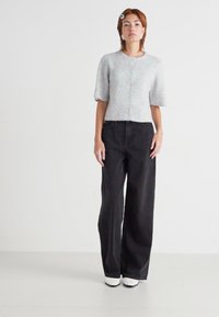 Grå strikket kortermet cardigan med knapper, kombinert med høy midje svart vide jeans og hvite sko. Enkel design, uten mønstre.