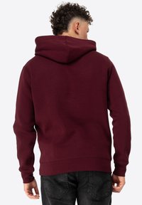 Bordeaux hoodie met een zachte textuur, kangoeroezak en verstelbare trekkoordcapuchon. Ontworpen met een relaxte pasvorm en geribbelde manchetten.