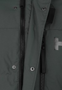 Chaqueta gris oscuro con una tela texturizada, cremallera negra, botones a presión y un detalle de logotipo en un acabado metálico en la parte frontal.