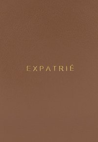 Copertina in pelle marrone con la parola "EXPATRIÉ" in rilievo dorato, caratterizzata da una finitura testurizzata e un design minimalista.
