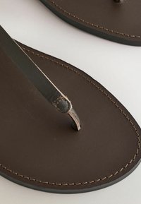 Sandale tongs en cuir marron avec coutures visibles le long des bords de la semelle sur un fond clair.