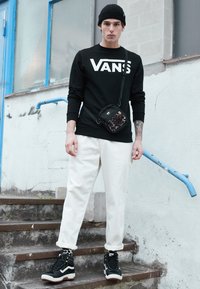Czarna bluza Vans z dużym logo, białe zwężane spodnie, czarno-białe sneakersy za kostkę oraz mała torba na ramię z akcentami w panterkę.