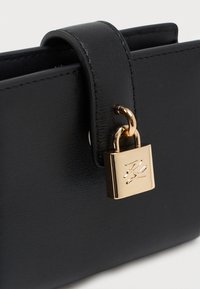 Portofel din piele neagră cu textură netedă, având un închizător auriu și decorat cu o curea cu buclă pentru o închidere securizată.