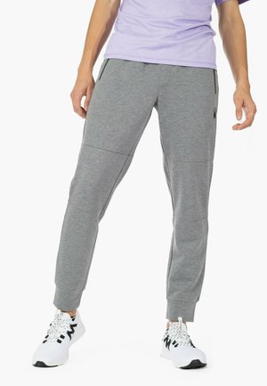 Pantalones deportivos grises con un patrón texturizado, que cuentan con bolsillos laterales con cremallera y puños acanalados, combinados con zapatillas blancas con acentos negros.