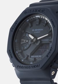 G-SHOCK klokke med et matt marineblått resin hus, analog og digital skjerm, fremtredende hvite visere og teksturerte detaljer. Vanntett opp til 20 bar.