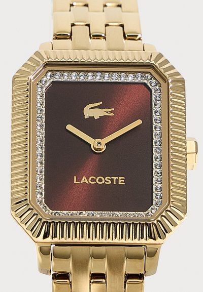Златист правоъгълен часовник Lacoste с кафяв циферблат, кристална рамка, златисти стрелки и златист метален верижен гривна.