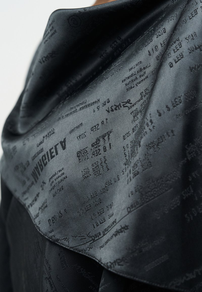 Tessuto di raso nero con un motivo testurizzato di testo stampato. Superficie liscia con sfumature e profondità variabili, che mette in evidenza i dettagli tipografici.