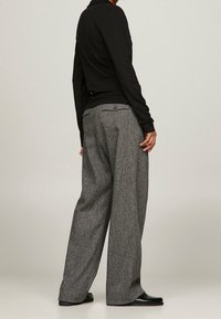 Grau melierte Hose mit weitem Bein und Gesäßtaschen, kombiniert mit einem enganliegenden schwarzen Langarmshirt.