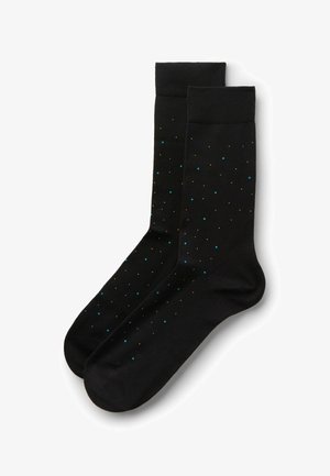 Paire de chaussettes noires montantes avec de petits pois épars bleus, blancs et orange, pliées côte à côte sur un fond blanc.