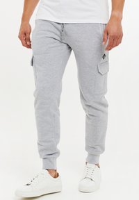 Grå mjukisbyxor med avsmalnande passform, sidofickor med lock och elastiska muddar; matchade med vita sneakers. Tillverkade av mjukt bomullsblandat material.